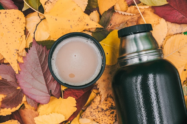 Foto una tazza di caffè con un thermos sullo sfondo delle foglie autunnali