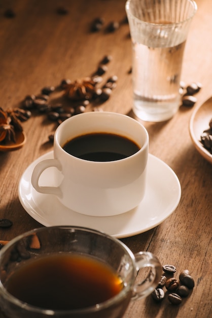 A cup of coffee with water, coffee beans and tea on wooden surface