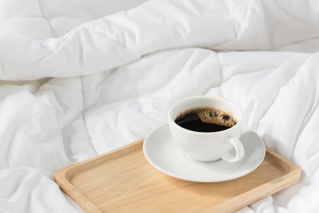 Cup of coffee with wooden tray on bed