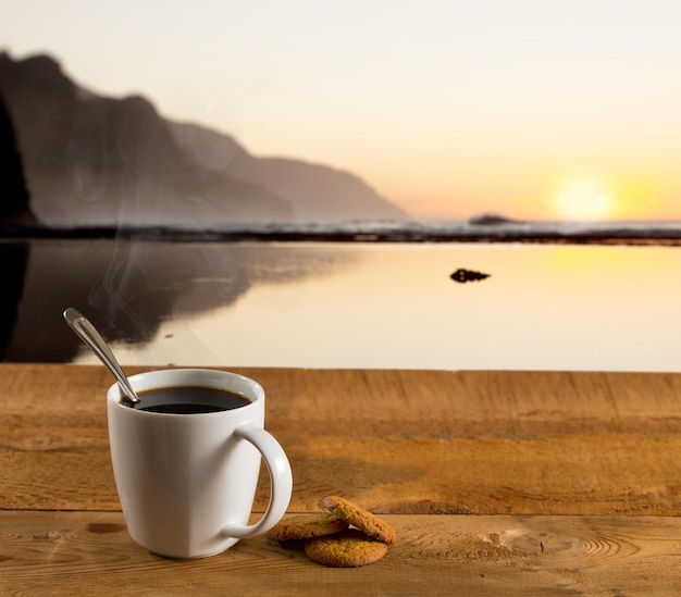 Cup of coffee on wooden table by ocean