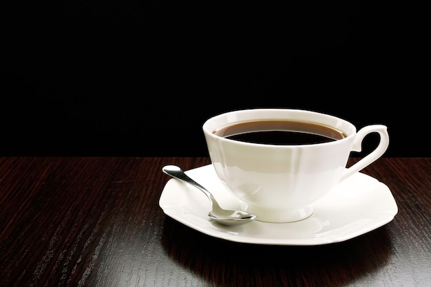 Cup of coffee on wooden table on dark background