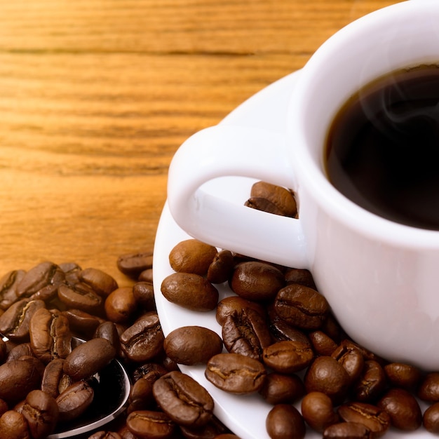 A cup of coffee on a wooden table among scattered freshly roasted coffee beans