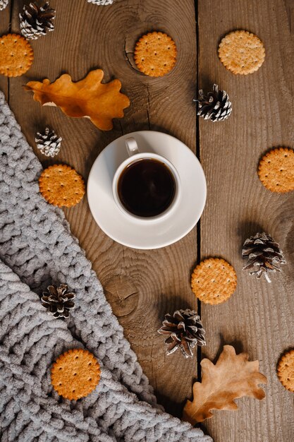 A cup of coffee on a wooden table with cookies, leaves and cones