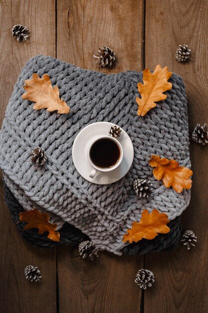 A cup of coffee on a wooden table with cookies, leaves and cones