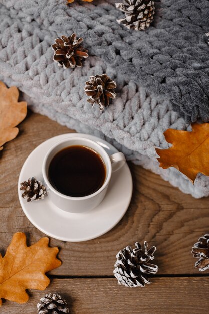 A cup of coffee on a wooden table with cookies, leaves and cones