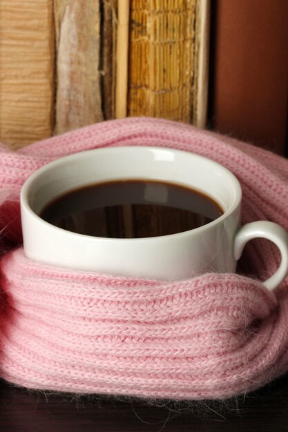 Cup of coffee wrapped in scarf on books background