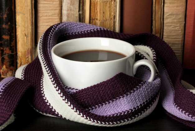 Cup of coffee wrapped in scarf on books background