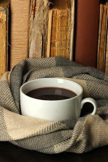 Cup of coffee wrapped in scarf on books