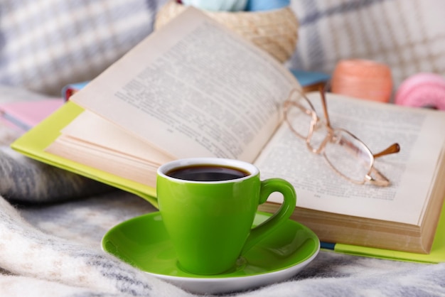 Cup of coffee and yarn for knitting on plaid with books closeup