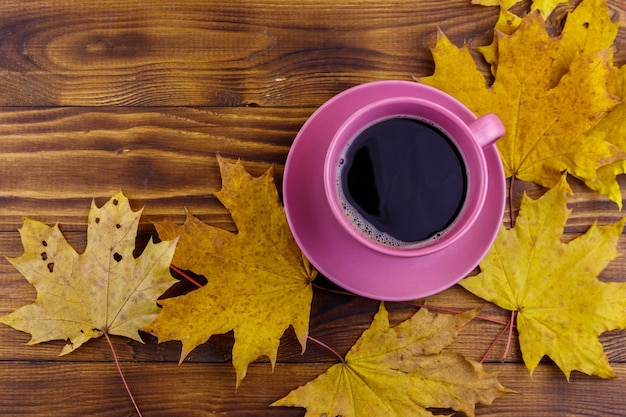 Cup of coffee and yellow maple leaves on wooden table Top view