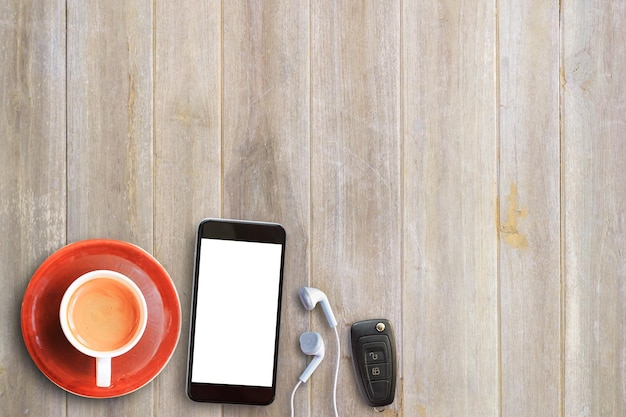 Cup of coffeesmart phoneear phone and car key on wooden