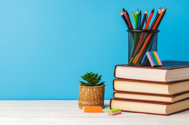 Cup of color pencils and stack of books on table