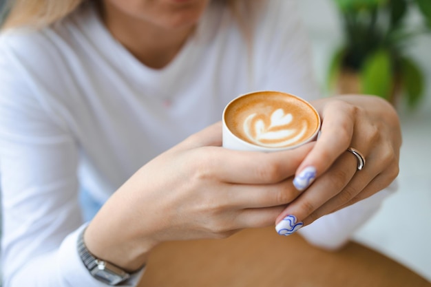 Cup of creamy cappucino coffee in woman hand's. Close up view of girl holding cup with aroma coffee