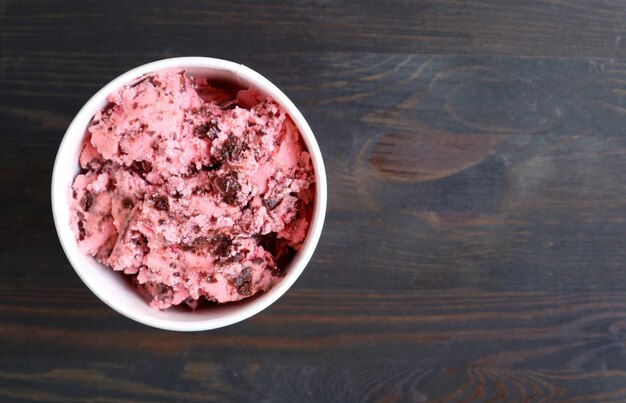 Cup of creamy strawberry chocolate chunk ice cream on dark brown wooden background