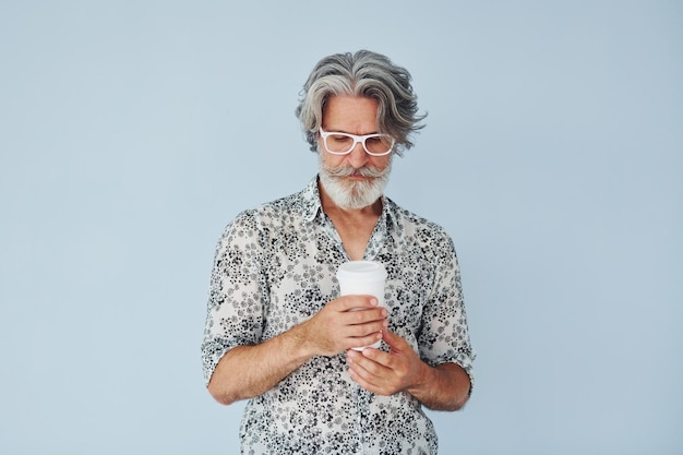 Чашка напитка в руках Старший стильный современный мужчина с седыми волосами и бородой в помещении