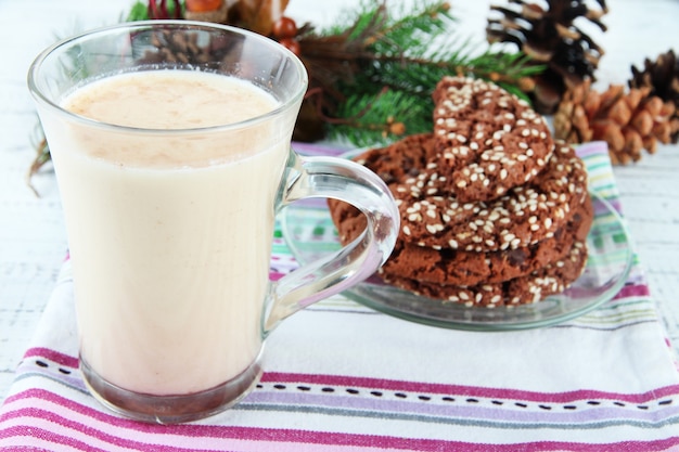 Cup of eggnog with cookie and fir branches on table close up