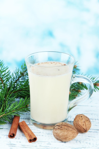 Cup of eggnog with fir branches on table on bright background