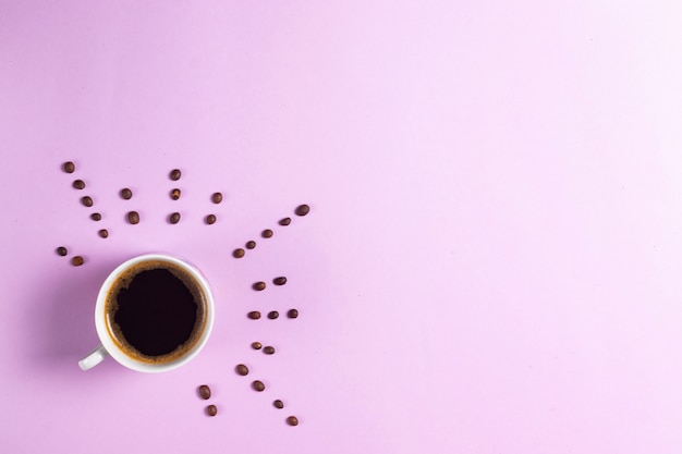 Cup of espresso coffee on a pink background with rays from coffee beans copyspace