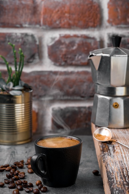 Tazza di caffè espresso, vapore sale sopra la tazza, una caffettiera e chicchi di caffè su un tavolo di pietra grigia, muratura. primo piano, pausa caffè o colazione, tempo del caffè