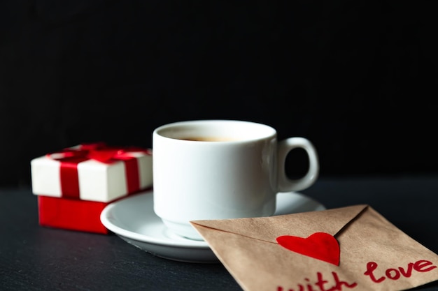 Cup of espresso coffee with gift and valentine. Black background, selective focus.