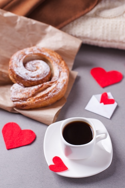 A cup of espresso on a saucer and a puff pastry, surrounded by hearts 
