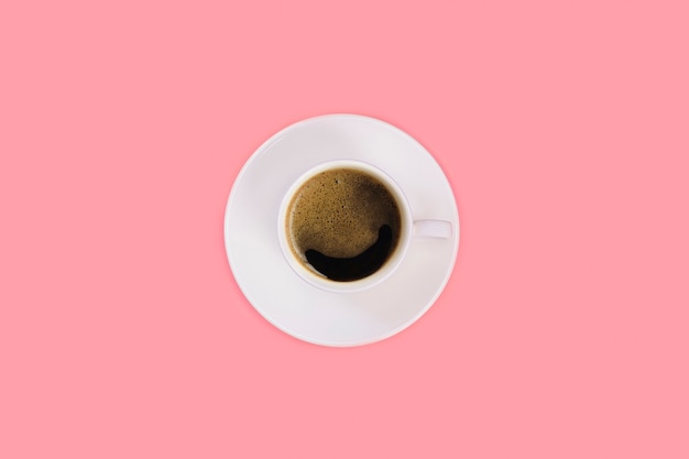 Cup of espresso on a white saucer on a pink background. Top view, flat lay, copy space