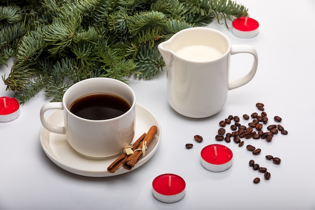 Cup of espresso with milk, cinnomon sticks, fir trees, red candles and on a white background