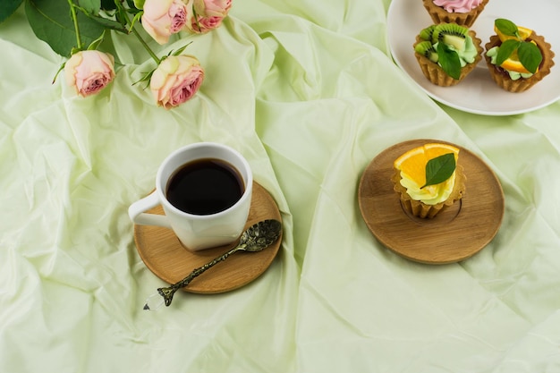 エスプレッソのカップ、プレートにクリームとフルーツが入ったミニトルティーヤ、バラの花束。ロマンチックな朝食。パステルカラーの背景。