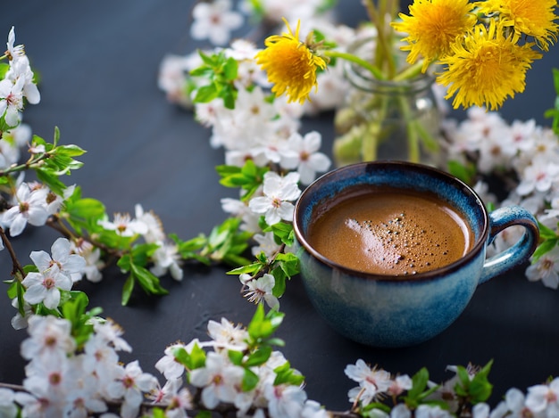 A cup of fragrant coffee, cherry blossoms, blooming yellow dandelions