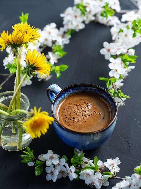 A cup of fragrant coffee, cherry blossoms, blooming yellow dandelions