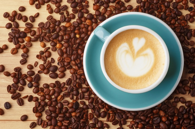 A cup of fragrant coffee in foam on a wooden table. Latte art. Coffee beans.