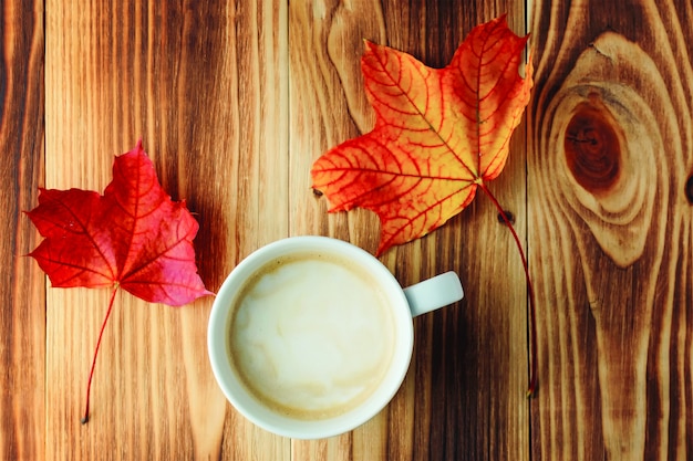 Чашка ароматного кофе и две осенние яркие кленовые листья
