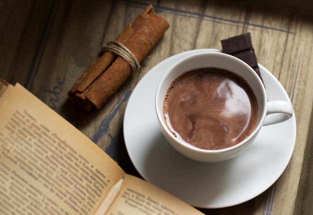 Cup of fragrant hot cocoa drink on a wooden tray with a book, cinnamon, cookies and chocolate