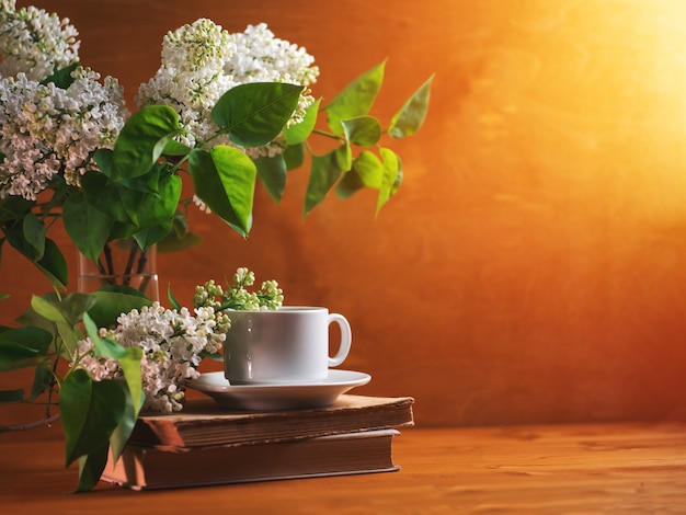 A cup of fragrant tea or coffee, a blooming white bouquet of lilacs and old books. Copy space morning breakfast