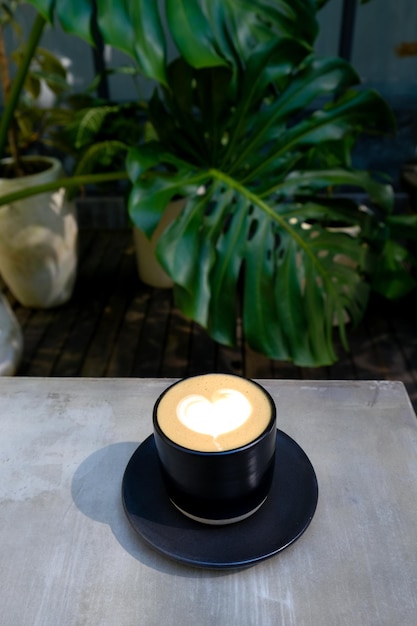 熱帯植物と木製のテーブル背景に新鮮なカプチーノ コーヒーのカップ