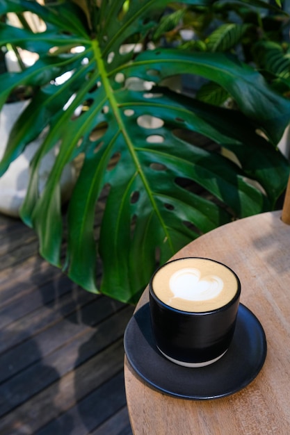 열대 식물이 있는 나무 테이블 배경에 신선한 카푸치노 커피 한 잔