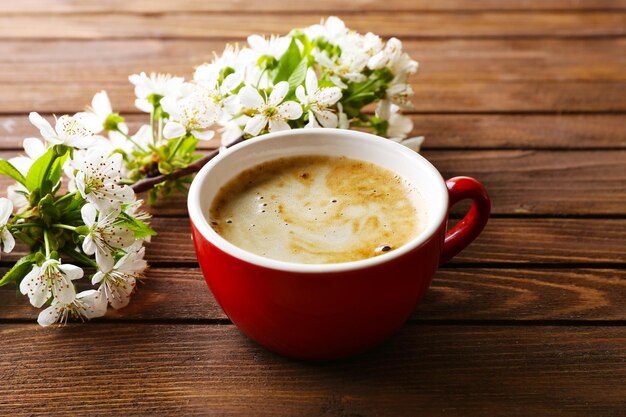 Cup of fresh coffee and blooming branch on wooden background