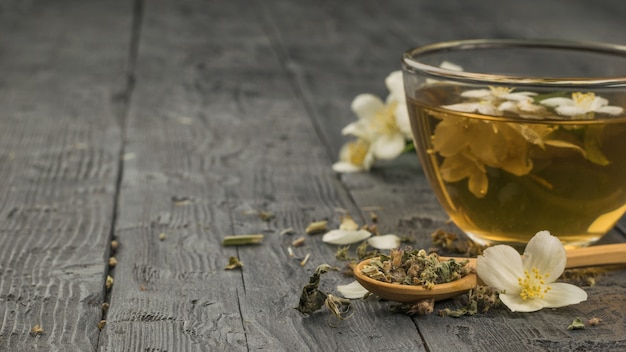 A cup of fresh tea with jasmine flowers on a black wooden table. Place for text.