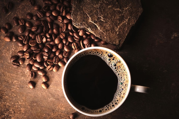 Cup of freshly brewed roasted coffee beans on brown background