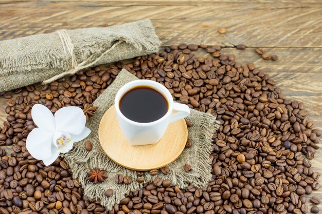 Una tazza di caffè aromatico appena preparato su un tavolo di legno con un fiore di orchidea e chicchi di caffè. composizione del caffè mattutino in campagna.