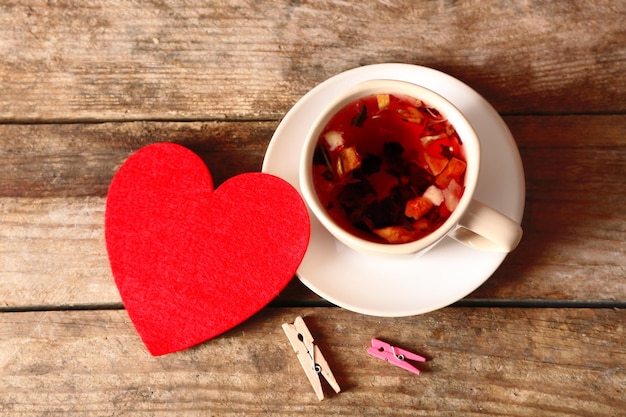 Cup of fruit tea with red heart and clothespins on wooden background closeup