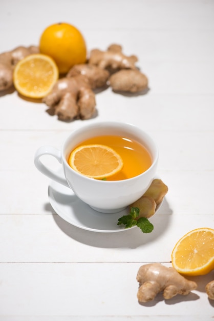 Tazza di tè allo zenzero con limone e miele su uno sfondo di legno bianco.