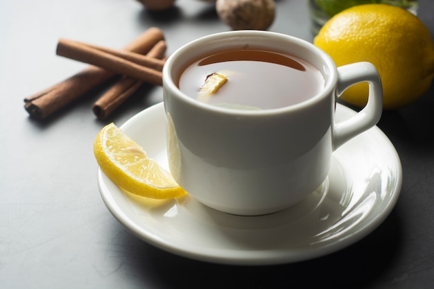 Cup of ginger tea with lemons and mint leaves on dark surface,