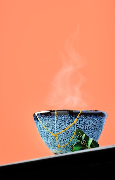 Cup of green japanese tea against a background of burnt sienna. Selective focus on cup. Steam rises above the bowl. Reclaimed ceramic blue cup, second life of things, recycling or kintsugi