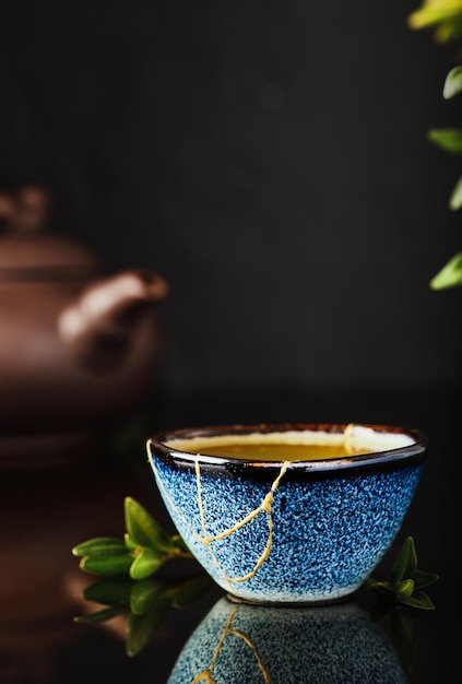 Cup of green Japanese tea on a dark background. Selective focus on the cup. Reclaimed ceramic blue cup, second life of things, recycling or kintsugi