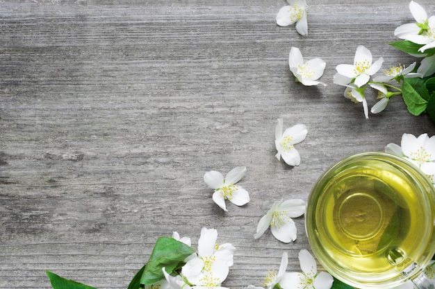 Cup of green jasmine tea and jasmine flowers on rustic wooden\
background