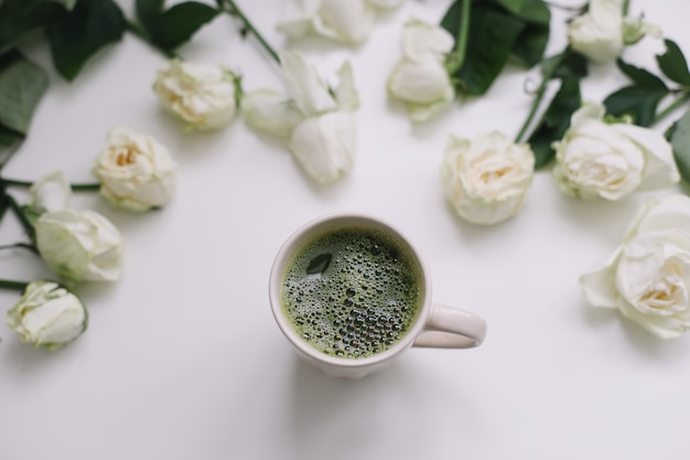 A cup of green matcha tea with white roses on white  view from above