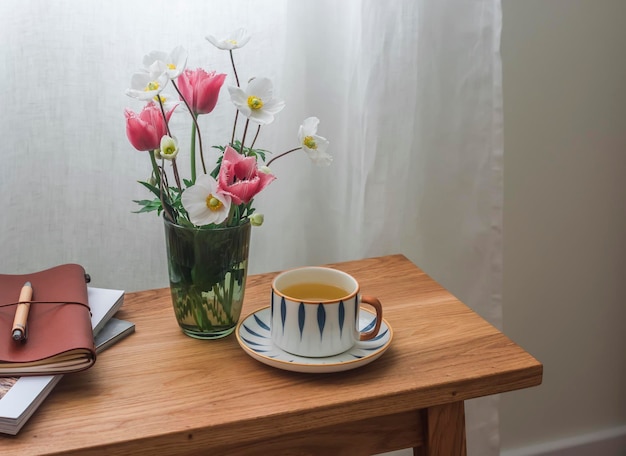 一杯の緑茶 春の庭の花の花束 居心地の良いリビングルームの木製テーブルの上のノート ゆっくりとしたお茶会