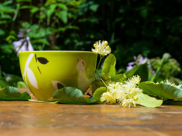 緑茶とリンデンの木製の背景、便利なリンデンの花民間療法の概念のカップ