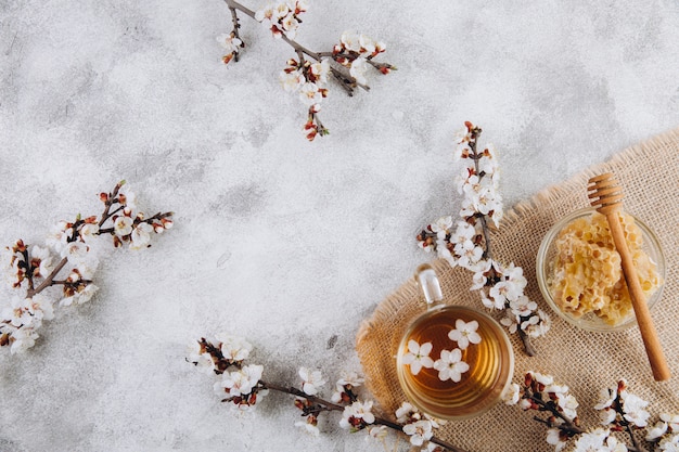 A cup of herbal tea and a jar of honey on a grey background